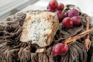 A piece of blue Stilton cheese on a wooden antique background with large red grapes. Close up